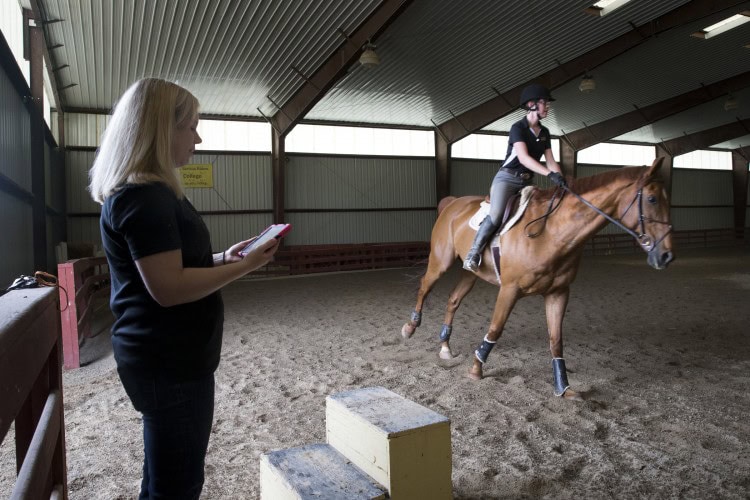 MacKenzi Brown rides one of the horses (Charlie) involved in her Summer Research project while professor Amanda Rumore tracks readings on an iPad.