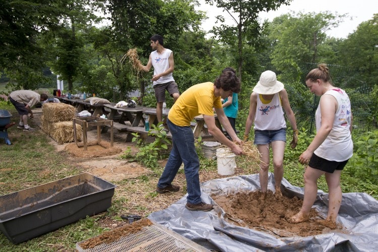 Environmental Studies Professor Karin Warren and Sara Woodward '16 mix up a batch of cob as Sustainability Coordinator Ludo Lemaitre (center) adds more straw on the tiny house site near the organic garden.