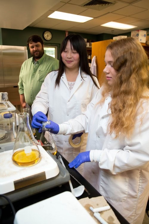 Biology professor Adam Houlihan observes as Di Bei '18 and Jacquelyn Parman '18 test lab samples.