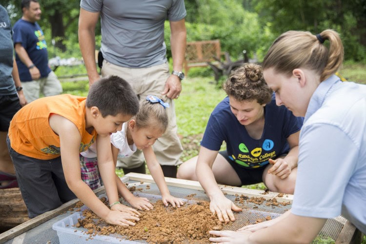 Jessy Spencer ’18 and sustainability coordinator Sara Woodward ’16 filter clay with children at the straw bale workshop in Randolph’s Organic Garden last week.