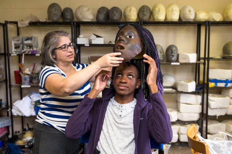 Director Amy Cohen helps Jordann Pruitt '19 put on his mask for the Greek Play.