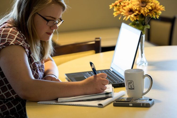 A student taking notes next to her laptop A student taking notes next to her laptop