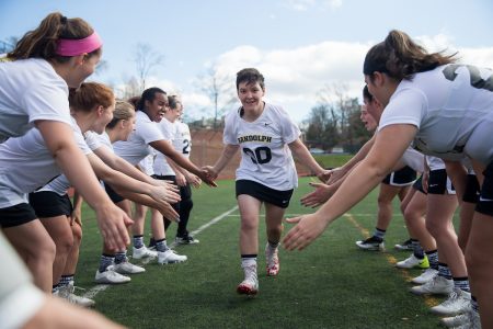 Women's lacrosse teammates form a tunnel and give five to a teammate running through