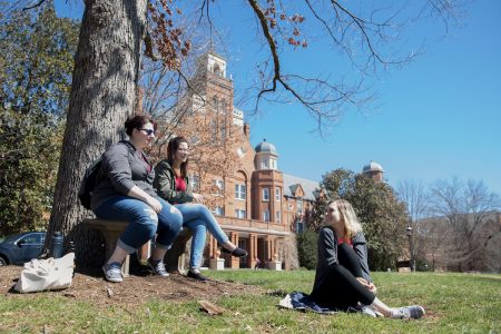 Three female students sitting and hanging out in front of Main Hall