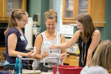 Teachers apply lotion to a plastic tube for an experiment on biofilm bacteria.