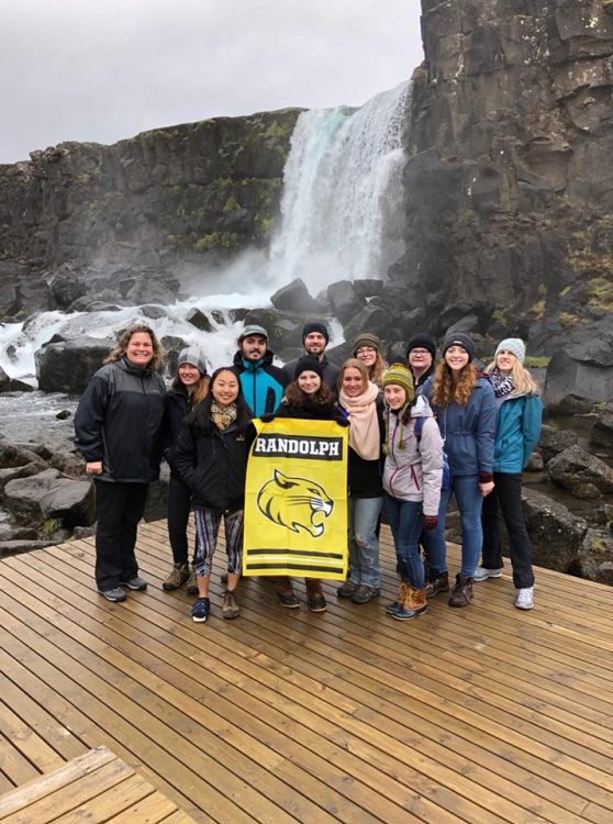 Students and faculty hold a Randolph banner in front of a waterfall in Iceland