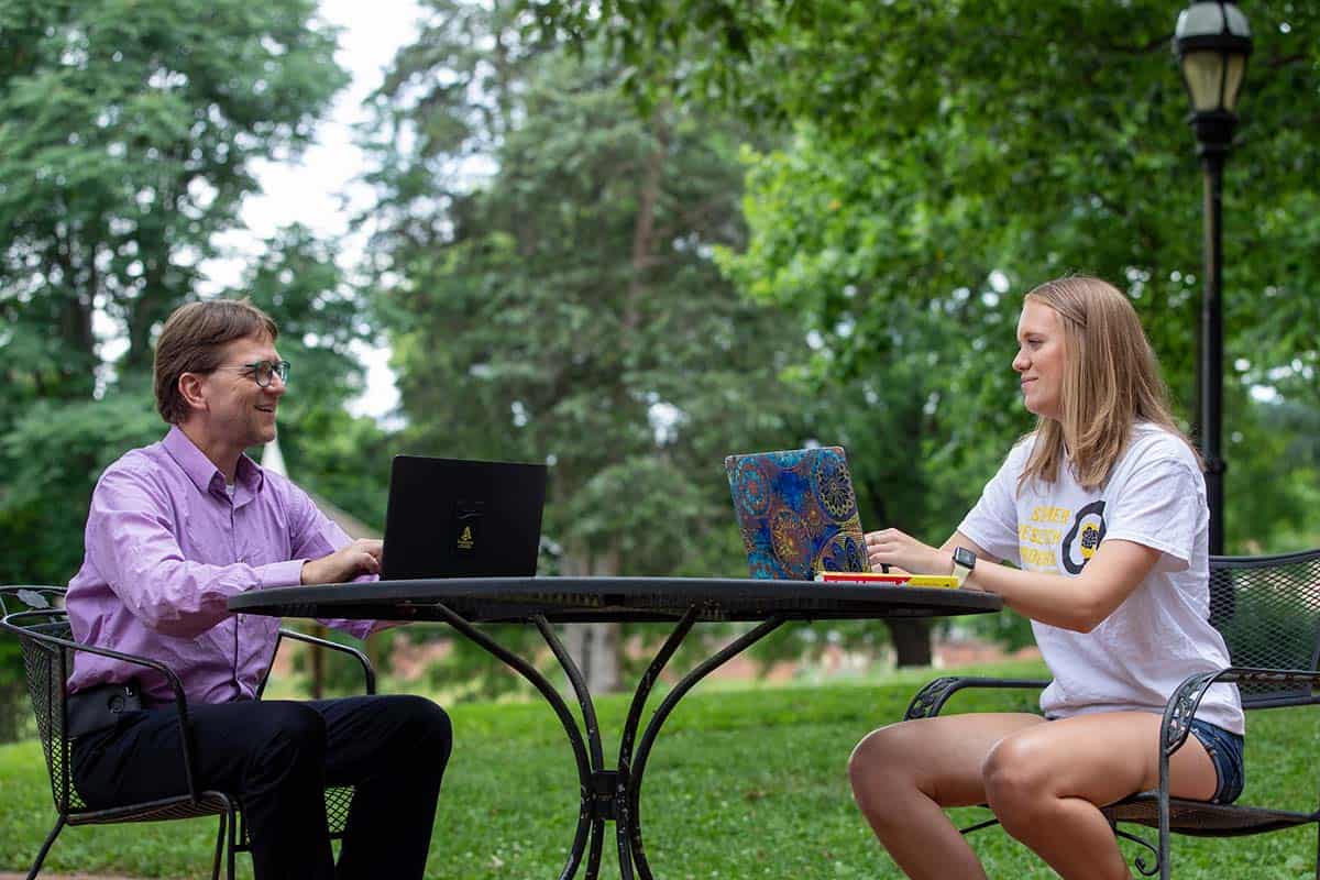 Professor Peter Sheldon meets with a student at an outdoor table.