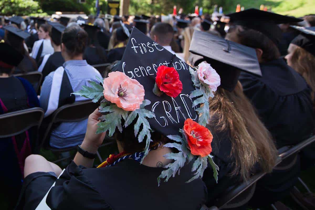 Graduating student wears a cap decorated with flowers and the words First Generation Grad.