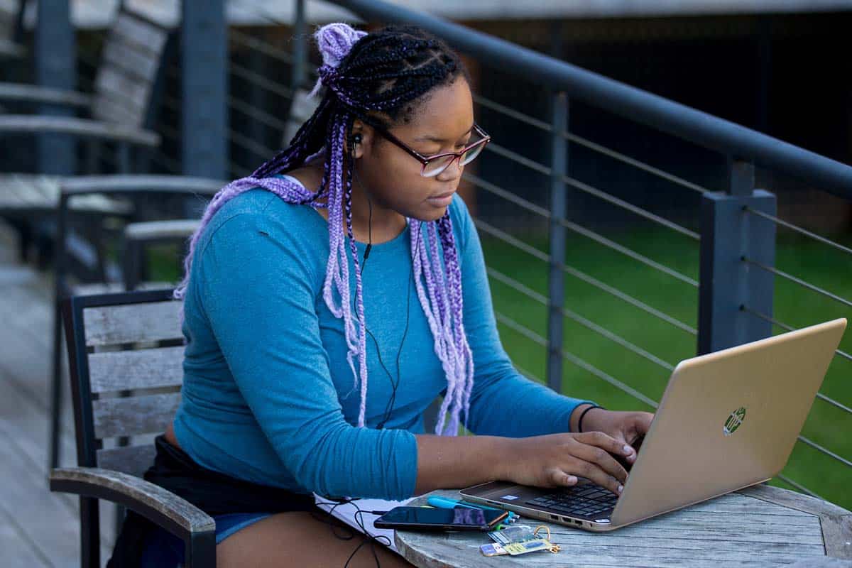 Female student works on her wi-fi connected laptop on the patio outside the Student Center.