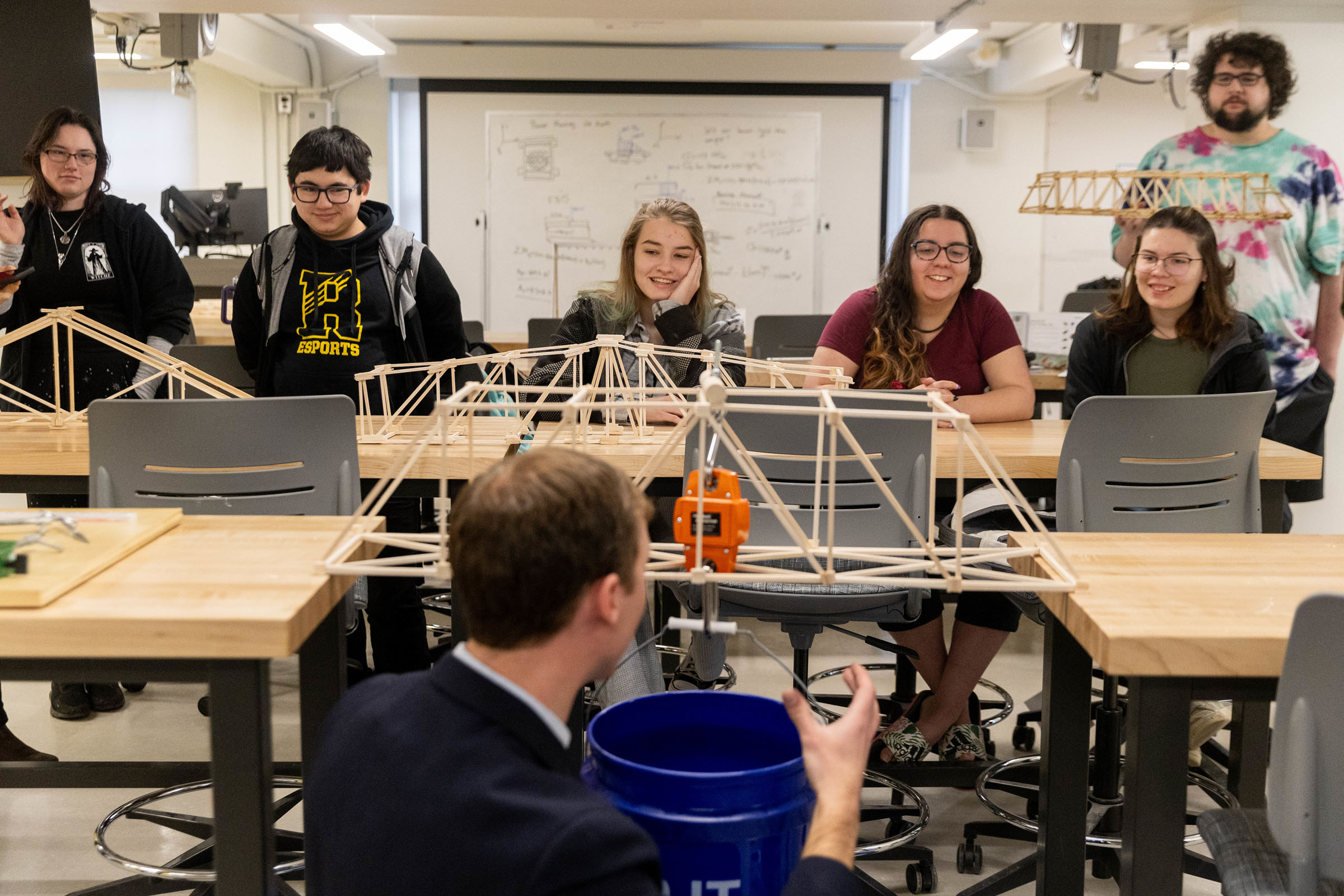 Randolph College engineering students watch as Professor Jonathan Skelton demonstrates how the they will test the strength of their bridge models.