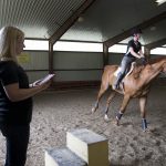 MacKenzi Brown rides one of the horses (Charlie) involved in her Summer Research project while professor Amanda Rumore tracks readings on an iPad.