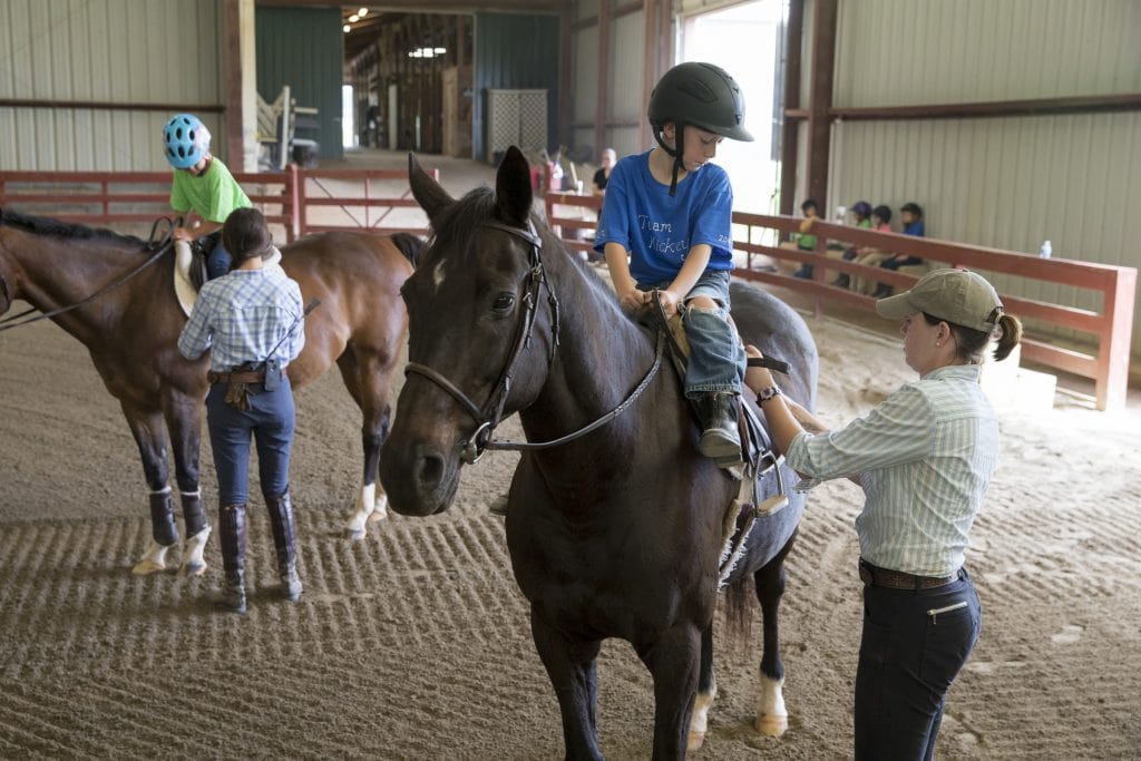 Camp volunteers help children saddle up.