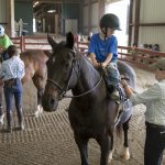 Camp volunteers help children saddle up.