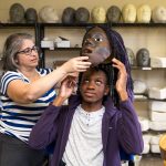 Director Amy Cohen helps Jordann Pruitt '19 put on his mask for the Greek Play.