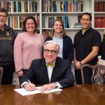 President Bradley W. Bateman signs the President's Resilience Commitment organized by Second Nature. Standing are (from left) Rick Barnes, professor of psychology and environmental studies and the Mary Sabel Girard Chair in Psychology; Sarah Sojka, professor of physics and environmental studies; Sara Woodward '16, sustainability coordinator; Michael Maningas, assistant dean of students; and Karin Warren, Herzog Family Chair of Environmental Studies.