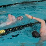 Two male teammates swim in opposite directions during a swimming practice.