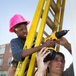 Austin Collier '19 helps a middle school student use a cordless drill while putting up walls for a tiny house.