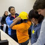 A Randolph student helps a middle schooler put on his yellow construction hat.