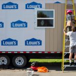 A middle schooler climbs the ladder against the tiny house and is handed a drill.