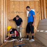 A middle schooler uses a drill inside the tiny house while a Randolph student and Vince Lowdermilk watch.