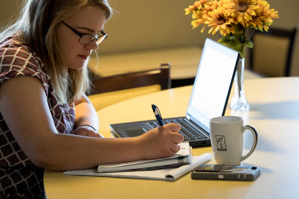 A student taking notes next to her laptop