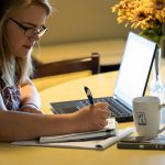 A student taking notes next to her laptop