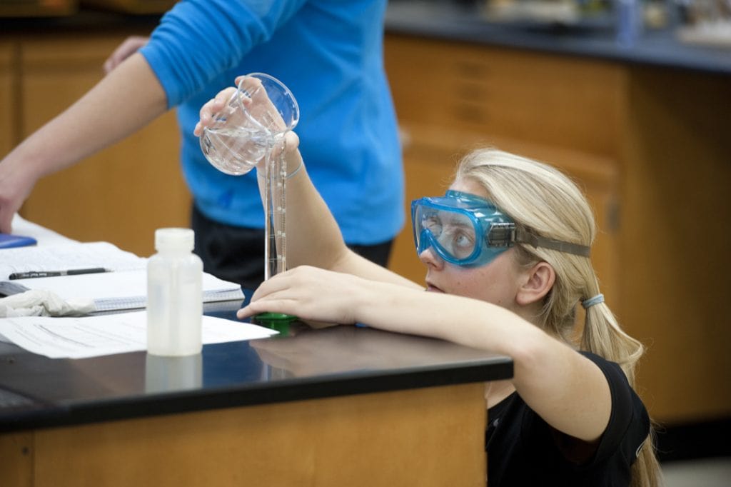 A student carefully measures liquid being poured into a beaker