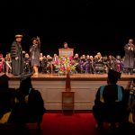 A graduate points at the crowd while walking across stage
