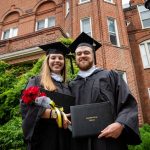 Two graduates pose in front of Main Hall