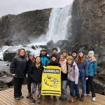 Students and faculty hold a Randolph banner in front of a waterfall in Iceland