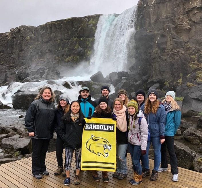 Students and faculty hold a Randolph banner in front of a waterfall in Iceland