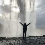 A student raises her hands in front of a waterfall