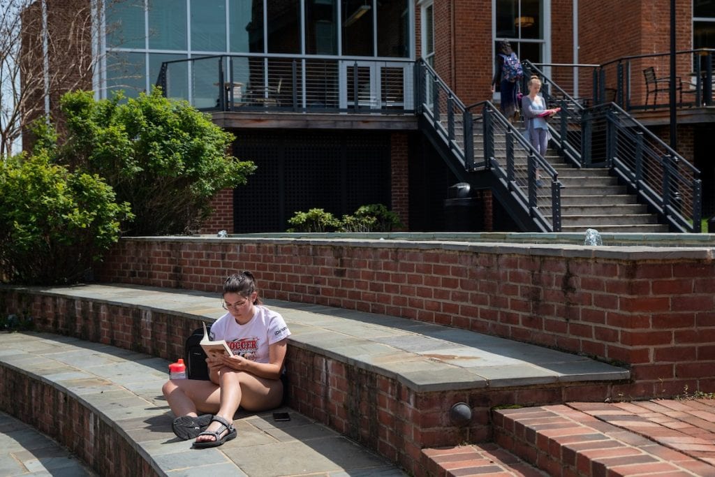 Female student reading a book in Michels Plaza with Student Center in the background