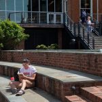 Female student reading a book in Michels Plaza with Student Center in the background