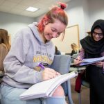 Two female students taking notes at their desks during class