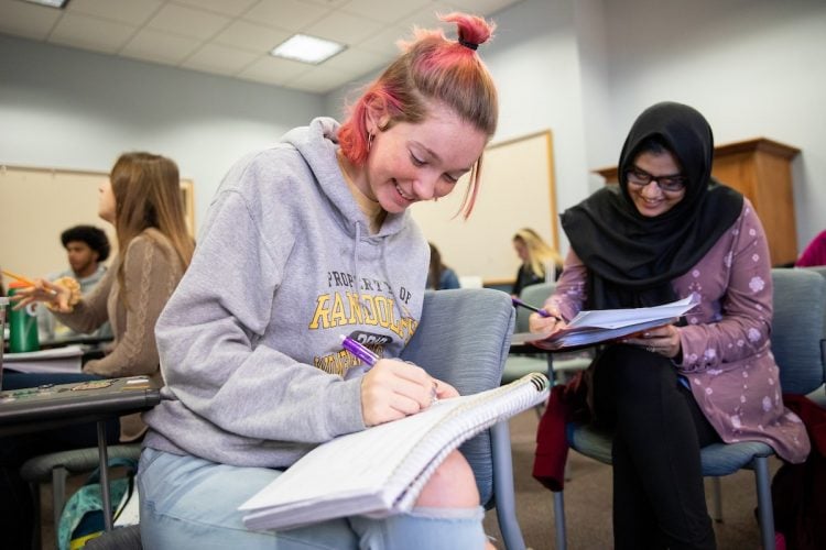 Two female students taking notes at their desks during class Two female students taking notes at their desks during class