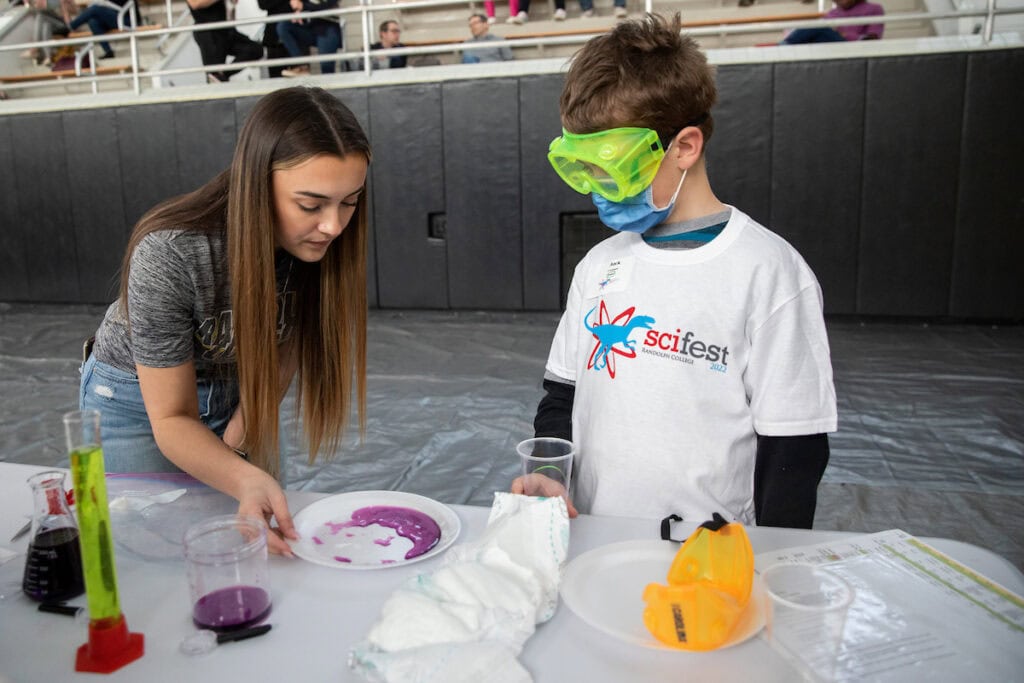 Female Randolph student teaches a science experiment to a young boy.
