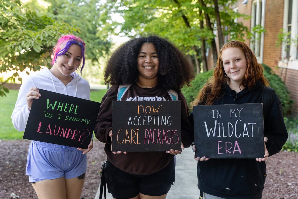 Three students stand together holding chalkboards that say 