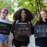 Three students stand together holding chalkboards that say 