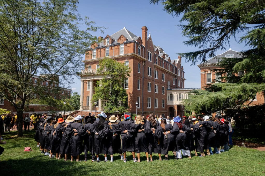 Students gather together, singing, around the Sundial after Convocation. This photo shows them from behind, arms around each other in a big circle.