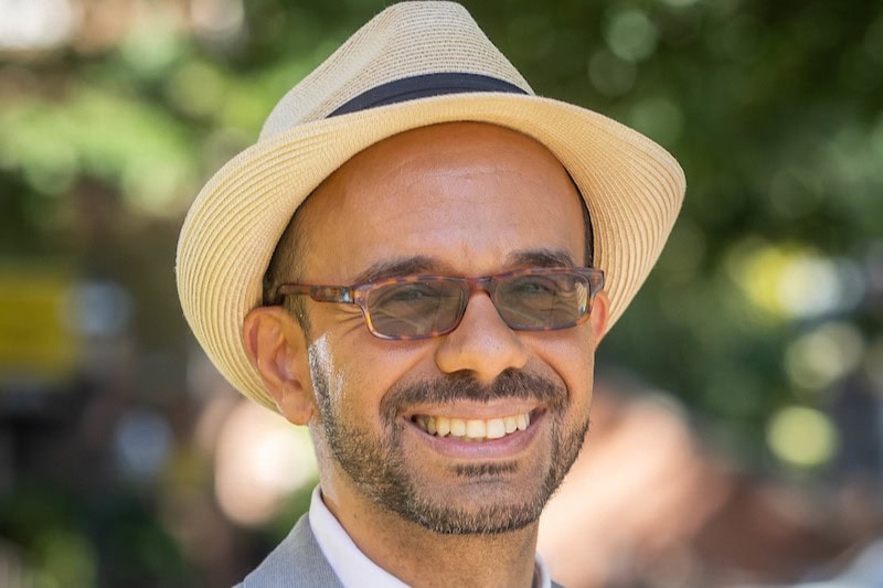 Alessandro Moscaritolo Palacio poses for a portrait photograph on front campus, wearing a straw hat