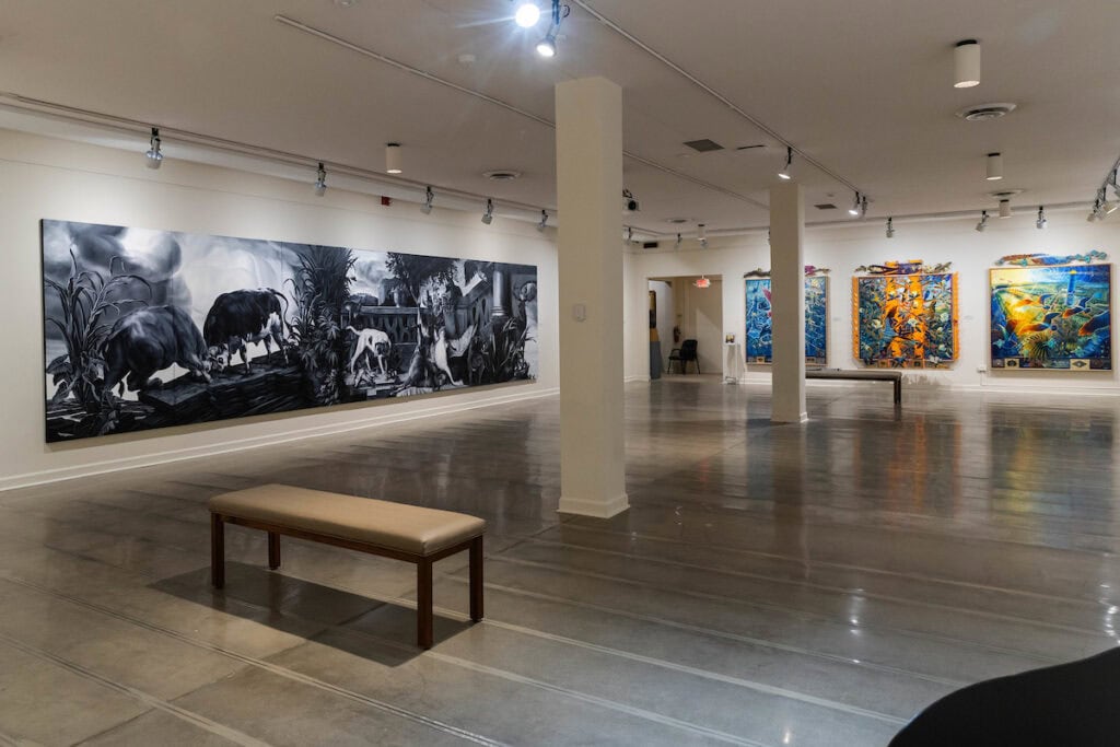 Photo inside the Maier Museum of Art at Randolph College, showing the new exhibition. A large-scale black and white drawing takes up the entirety of the left wall, while three colorful paintings hang on the back wall opposite. Photo inside the Maier Museum of Art at Randolph College, showing the new exhibition. A large-scale black and white drawing takes up the entirety of the left wall, while three colorful paintings hang on the back wall opposite.