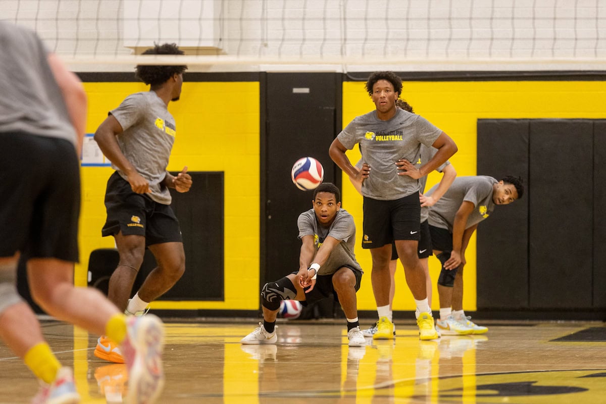 Members of the men's volleyball team practice in Randolph's athletic facility. One student in particular is crouched down, with his hands clasped together, about to hit the ball.
