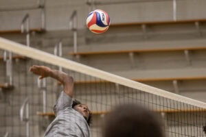 A player on the men's volleyball team jumps up , about the spike the ball over the net. 