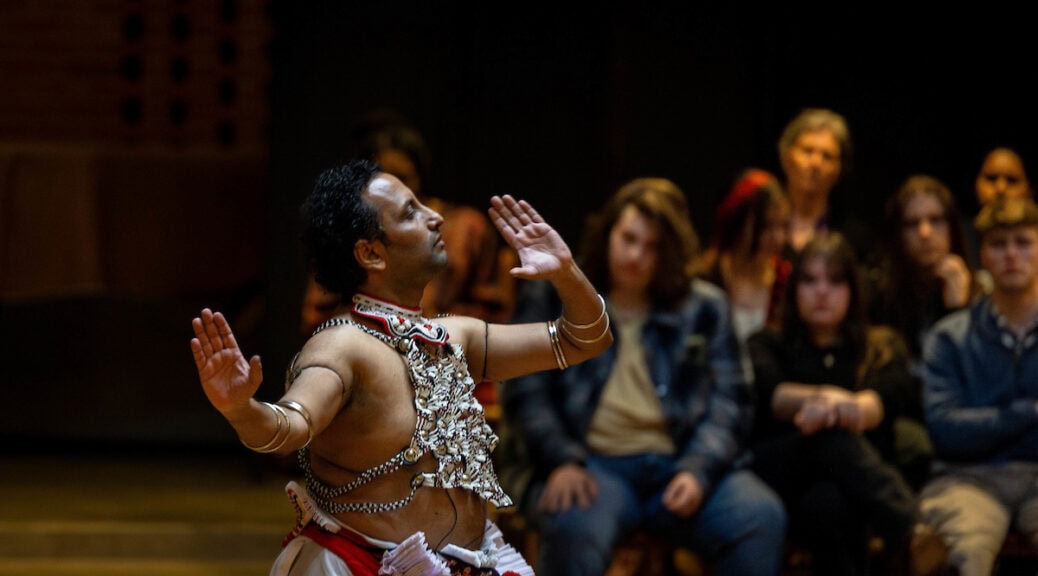 Sudesh Mantillake performs Kandyan dance in Houston Memorial Chapel. The photo is shot from the side, so you see his profile, with one hand raised above his head.