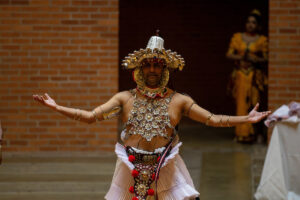 Sudesh Mantillake stands in the center of Houston Memorial Chapel, wearing traditional Kandyan dance garb, including a beaded chestplate, bangles on his arms, and a headpiece.