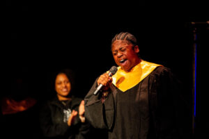Charmayne Wyche sings, holding a microphone, with Randolph's Gospel Choir 