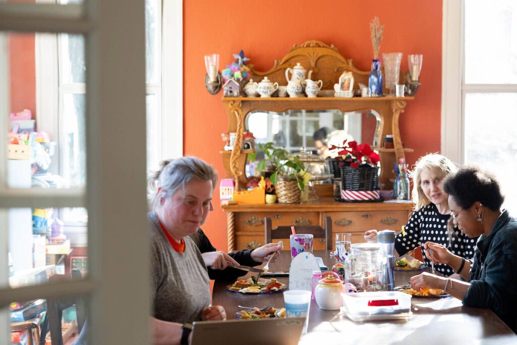 Professor Sarah Sojka sits at her kitchen table, opposite Elizabeth Parsons '25 and colleague Karin Warren, as they share a meal together.