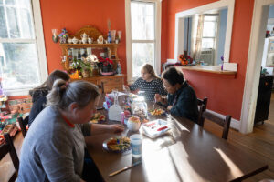 Professor Sarah Sojka sits at her kitchen table, opposite Elizabeth Parsons '25 and colleague Karin Warren, as they share a meal together.