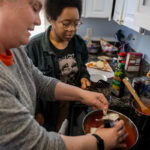 Sarah Sojka and Elizabeth Parsons cook together over a stovetop.